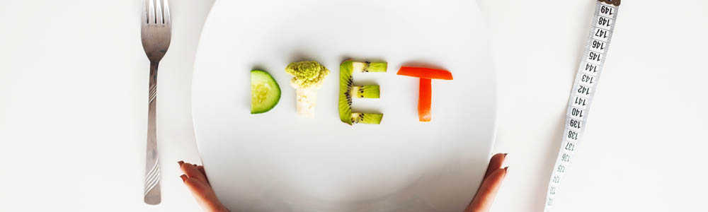 White plate with the word "diet" spelt out in vegetables, with a measuring tape wrapped around the plate and a fork beside it